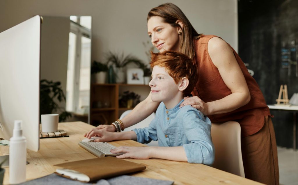 Eine Mutter und ihr Kind lächeln, während sie zu Hause am Computer sitzen und konzentriert etwas Neues lernen.