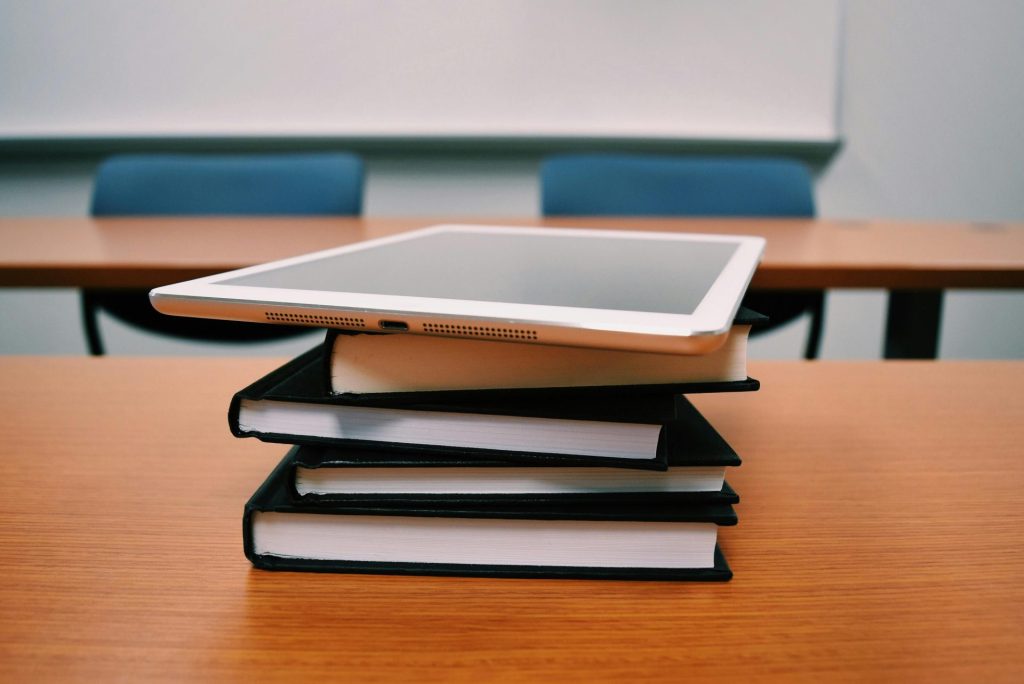 Ein Tablet liegt auf einem Stapel Bücher in einem leeren Klassenzimmer und veranschaulicht moderne Bildung.